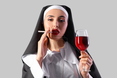Naughty nun with glass of wine smoking cigarette on light background, closeup