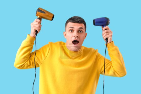 Photo for Surprised young man with hair dryers on blue background - Royalty Free Image