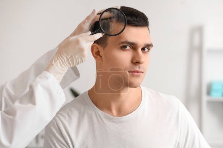 Photo for Trichologist with magnifier examining young man's hair in clinic, closeup - Royalty Free Image
