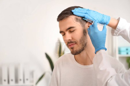 Photo for Young man with marked forehead receiving injection for hair growth at hospital, closeup - Royalty Free Image