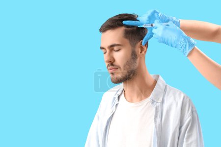 Photo for Young brunette man receiving injection for hair growth on blue background, closeup - Royalty Free Image