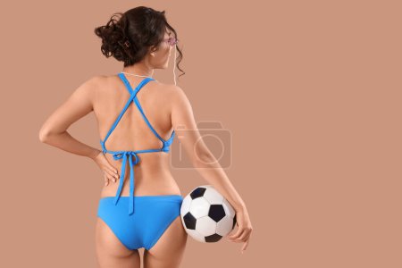 Sexy young woman in swimsuit and with soccer ball on beige background, back view