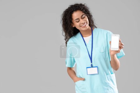 Afroamerikanische Medizinpraktikantin mit Handy auf hellem Hintergrund