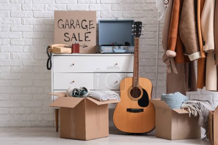 Photo for Many various unwanted things and cardboard with text GARAGE SALE near white brick wall in room - Royalty Free Image