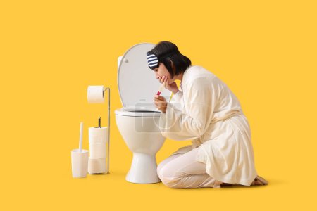 Téléchargez les photos : Sick young woman with pregnancy test near toilet bowl on yellow background - en image libre de droit