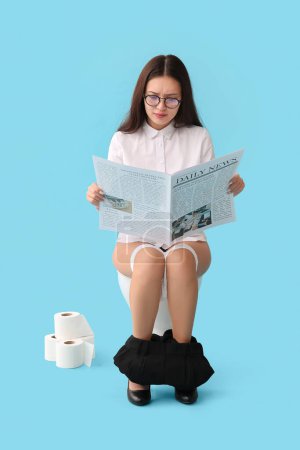 Téléchargez les photos : Jeune femme d'affaires asiatique lecture journal sur cuvette de toilette sur fond bleu - en image libre de droit