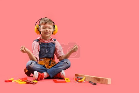 Téléchargez les photos : Mignon petit constructeur avec des outils jouets méditant sur fond rouge - en image libre de droit