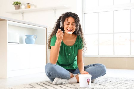 Téléchargez les photos : Belle jeune femme afro-américaine dans un casque avec panier de crème glacée assis sur le tapis à la maison - en image libre de droit
