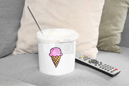 Téléchargez les photos : Panier de crème glacée sucrée et télécommande TV sur canapé - en image libre de droit