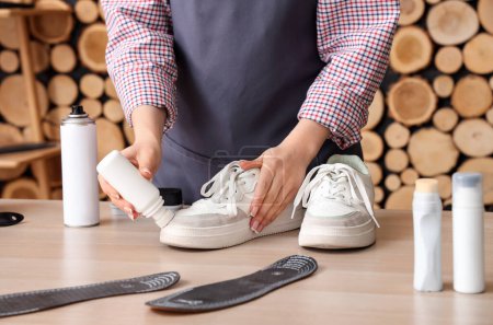 Photo for Female shoemaker cleaning stylish sneakers at wooden table, closeup - Royalty Free Image