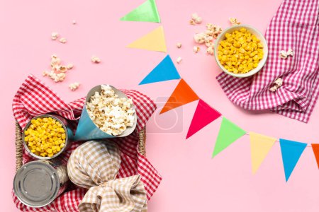 Foto de Composición con sabrosas palomitas de maíz, maíz y decoración para la celebración de Festa Junina sobre fondo rosa - Imagen libre de derechos