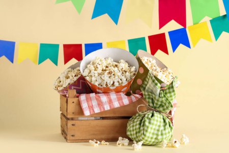 Holzkorb mit leckerem Popcorn, Bündeltasche und Fahnen für die Festa Junina auf farbigem Hintergrund
