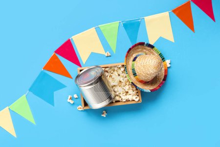 Wooden basket with popcorn, canned corn and decor for Festa Junina celebration on color background
