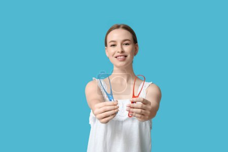 Young woman with tongue scrapers on blue background