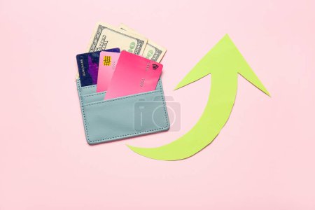 Cartera con tarjetas de crédito, dinero y flecha sobre fondo rosa. Concepto de aumento de precios