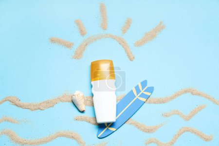 Composition with bottle of sunscreen cream, mini surfboard and sand on color background