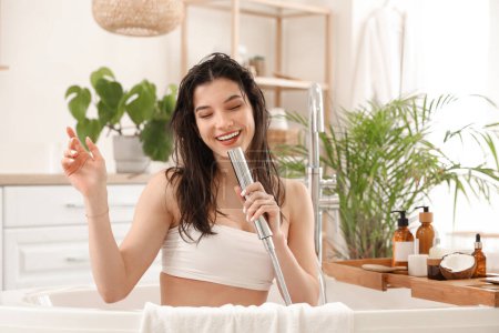 Téléchargez les photos : Belle jeune femme heureuse avec des bouteilles de masques capillaires chantant dans la salle de bain à la maison - en image libre de droit