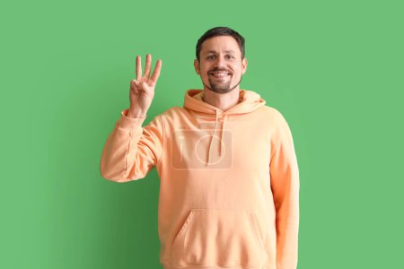 Foto de Hombre guapo mostrando tres dedos sobre fondo verde - Imagen libre de derechos