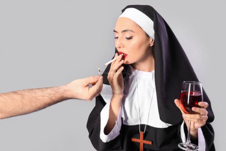 Sexy Nonne mit einem Glas Wein zündet Zigarette auf hellem Hintergrund an