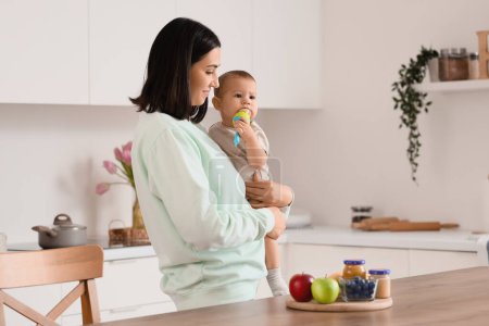 Madre dando a su pequeño bebé mordisquear con comida en la cocina