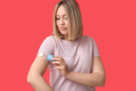 Femme avec capteur de glucose pour mesurer le taux de sucre dans le sang et applicateur sur fond rouge. Concept de diabète