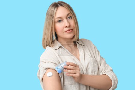 Woman with glucose sensor for measuring blood sugar level and applicator on blue background. Diabetes concept