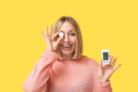 Frau mit Glukometer und Sensor zur Messung des Blutzuckerspiegels auf gelbem Hintergrund. Diabetes-Konzept