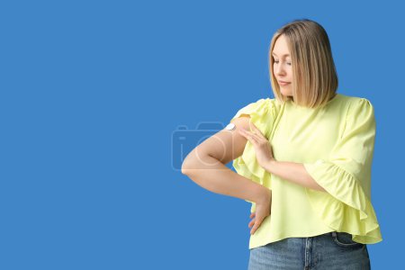 Woman with glucose sensor for measuring blood sugar level on blue background. Diabetes concept