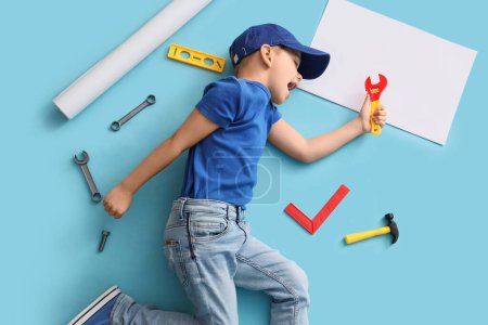 Téléchargez les photos : Mignon petit constructeur avec des outils jouet couché sur fond bleu, vue de dessus - en image libre de droit