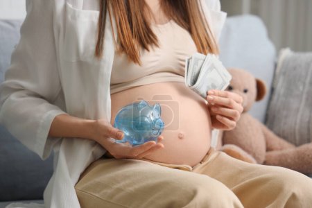 Young pregnant woman with money and piggy bank sitting at home, closeup. Maternal Benefit concept