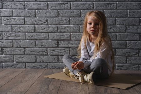 Photo for Homeless little girl sitting near grey brick wall - Royalty Free Image