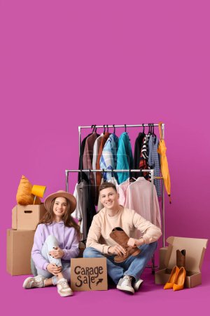 Photo for Young couple holding cardboard with text GARAGE SALE and boxes of unwanted stuff on purple background - Royalty Free Image