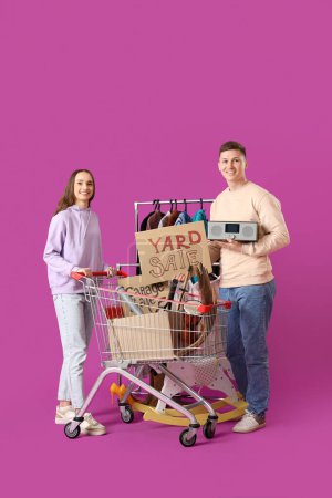 Photo for Young couple holding cardboard with text YARD SALE and unwanted stuff on purple background - Royalty Free Image