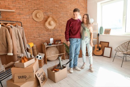 Photo for Young couple hugging in room of unwanted stuff. Yard Sale - Royalty Free Image