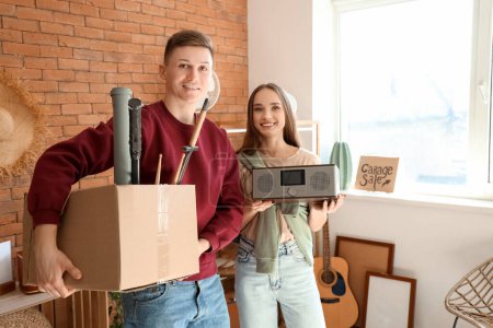 Photo for Young couple with box of unwanted stuff in room. Yard Sale - Royalty Free Image
