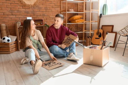 Photo for Young couple writing GARAGE SALE on cardboard in room of unwanted stuff - Royalty Free Image