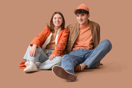 Photo for Young beautiful couple in stylish coats sitting on floor on beige background - Royalty Free Image