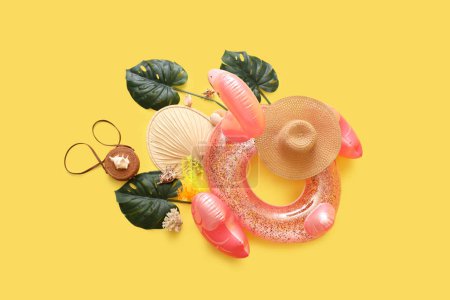 Beach accessories with inflatable ring, seashells and palm leaves on yellow background