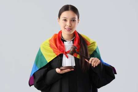 Photo for Female Asian judge with LGBT flag and gavel on light background - Royalty Free Image