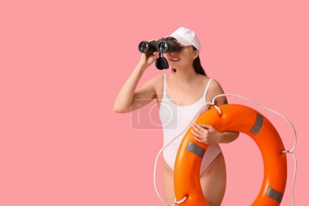 Photo for Young female lifeguard with ring buoy looking through binoculars on pink background - Royalty Free Image