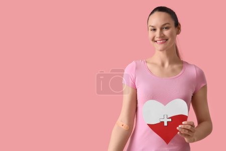 Female blood donor with applied patch and paper heart on pink background