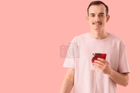 Male blood donor with applied patch and pack for transfusion on pink background