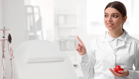 Female doctor with heart pointing at something in clinic. Banner for design