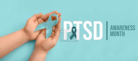 Hands holding ribbon on blue background. Post-Traumatic Stress Disorder Awareness Month