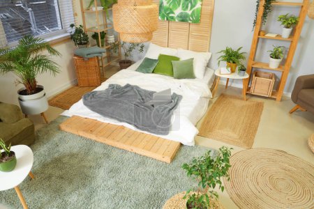 Téléchargez les photos : Intérieur de la chambre avec plantes vertes, étagères et ordinateur portable sur le lit - en image libre de droit