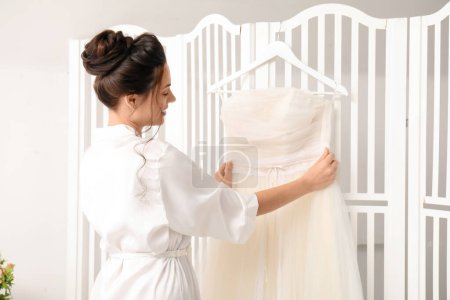 Foto de Joven novia con su vestido de novia colgando en la pantalla plegable en el dormitorio - Imagen libre de derechos