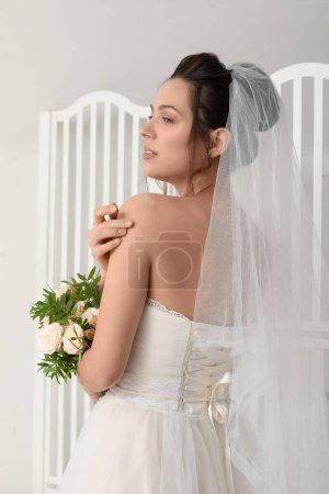 Téléchargez les photos : Jeune mariée avec bouquet de mariage près de l'écran pliant sur fond clair - en image libre de droit