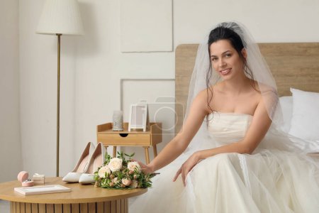 Foto de Hermosa novia joven con ramo de bodas sentado en el dormitorio - Imagen libre de derechos