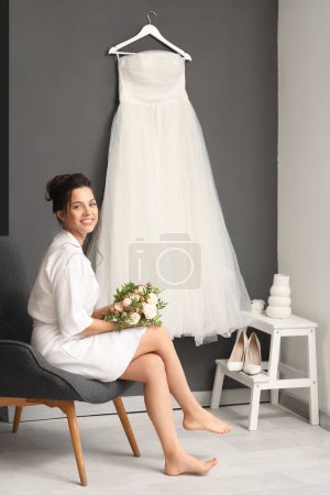 Foto de Hermosa novia joven con su ramo de bodas sentado en el vestidor - Imagen libre de derechos