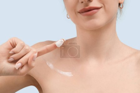 Photo for Young woman with cosmetic cream on her finger against blue background, closeup - Royalty Free Image